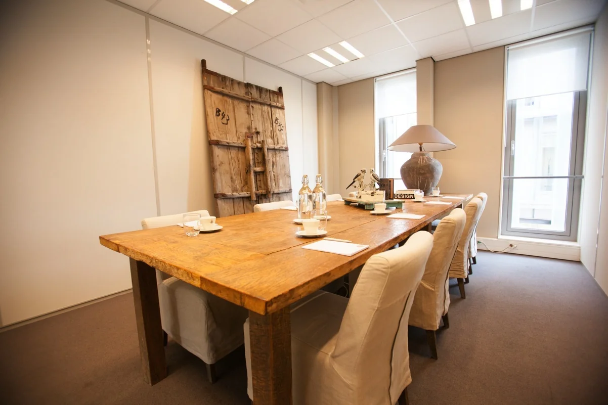 Vergaderruimte aan de Orteliuslaan met een grote houten tafel, omringd door stoelen en voorzien van waterflessen, kopjes en decoratie.