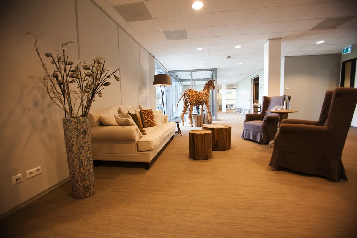 Moderne wachtruimte aan de Orteliuslaan met comfortabele zitplaatsen, houten decorpaarden en natuurlijke accenten.