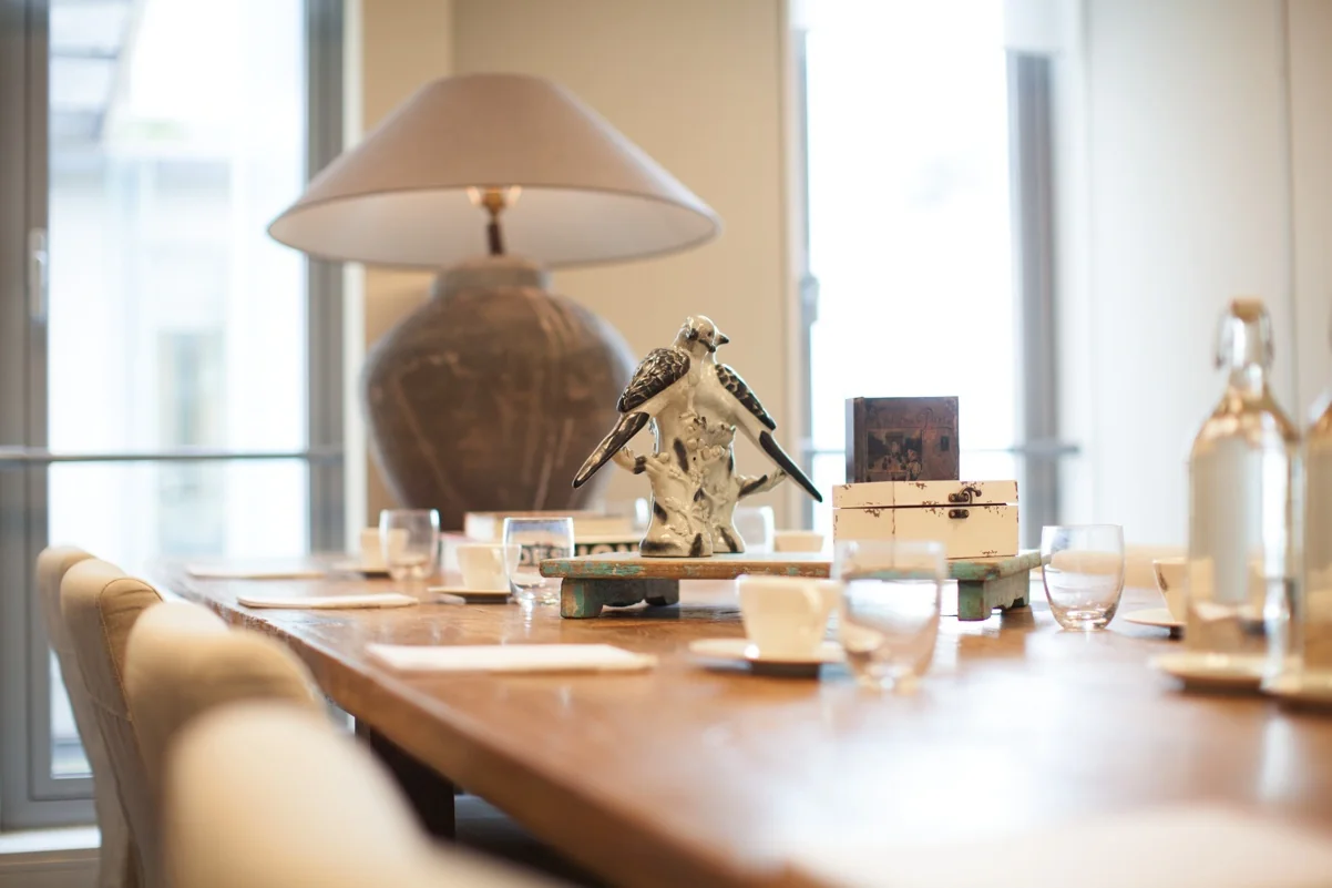 Vergadertafel met servies, decoratieve vogelbeelden en een grote lamp op de achtergrond in een ruimte aan de Orteliuslaan.
