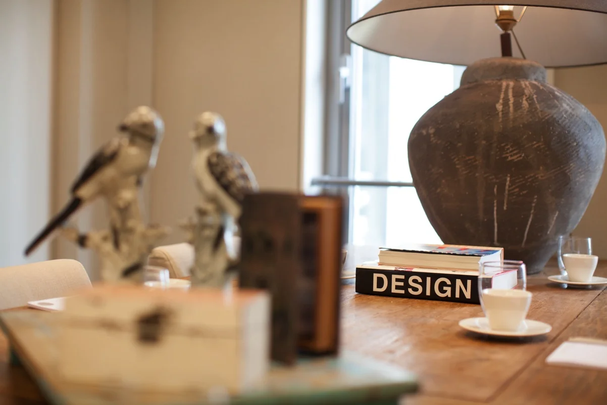 Houten tafel met boeken, koffiekopjes, keramische vogels en een grote designlamp in een stijlvol interieur aan de Orteliuslaan.