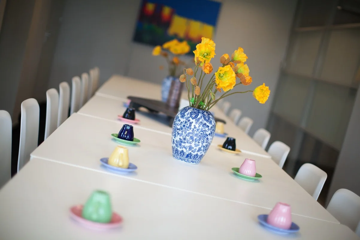 Lange vergadertafel met witte stoelen, kleurrijke kopjes en een vaas met gele bloemen in een moderne ruimte aan de Orteliuslaan.