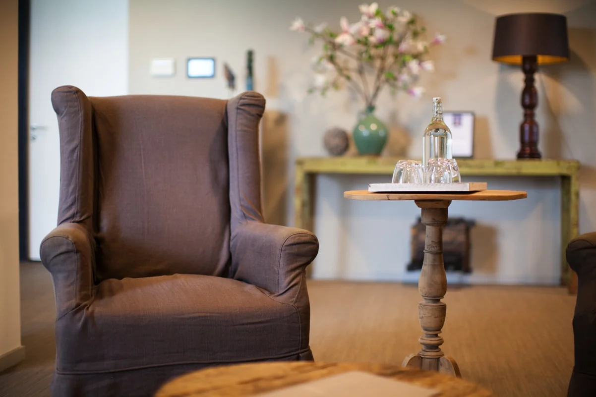 Comfortabele zithoek met een bruine fauteuil, een houten bijzettafel met waterfles en glazen, en een sfeervol ingerichte achtergrond in Orteliuslaan.