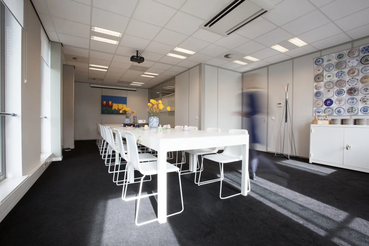 Vergaderruimte aan de Orteliuslaan met lange tafel, witte stoelen, bloemen op tafel en wanddecoratie met borden.