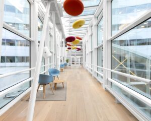 Lichte, moderne loopbrug met kleurrijke ronde plafondpanelen en zithoekjes langs de glazen wanden.