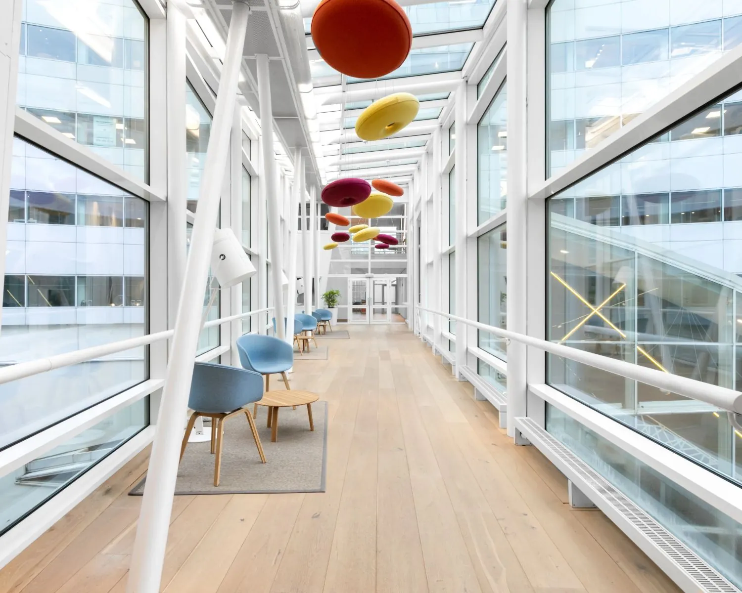 Lichte, moderne loopbrug met kleurrijke ronde plafondpanelen en zithoekjes langs de glazen wanden.