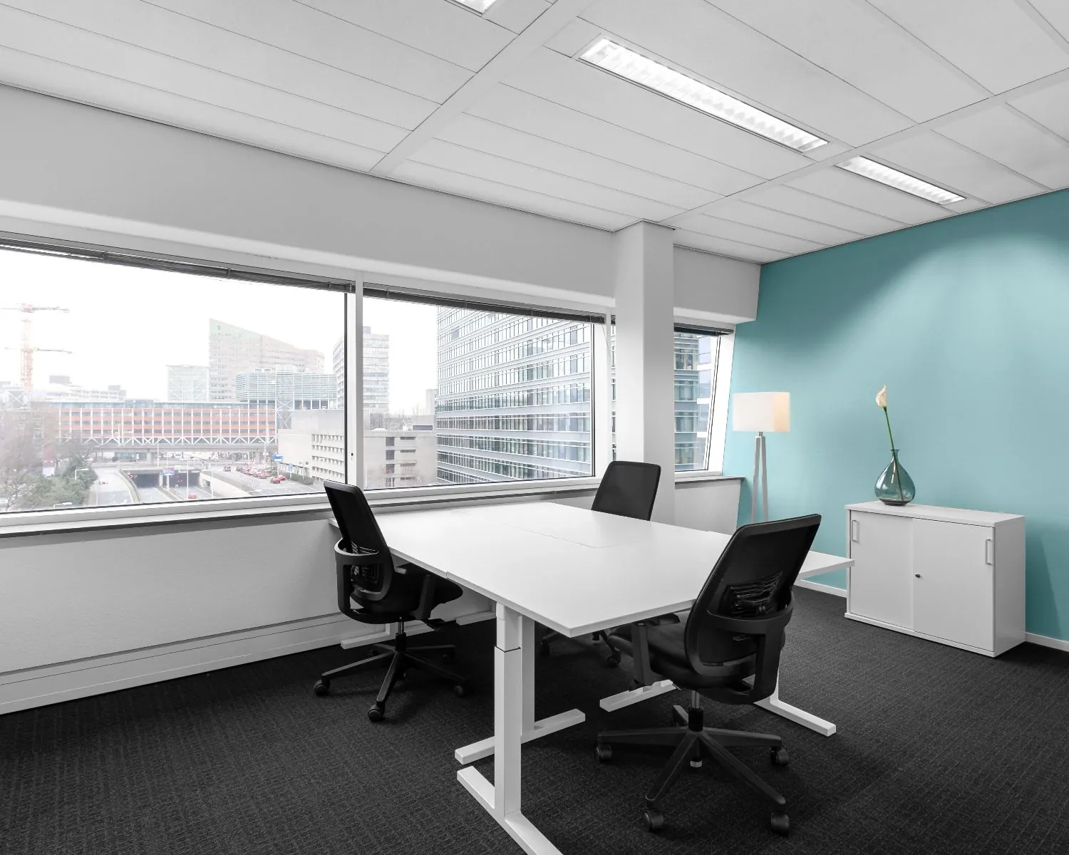 Moderne kantoorruimte met twee bureaus, bureaustoelen en uitzicht op een stedelijk zakendistrict.