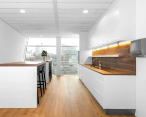 Moderne witte kantoorkeuken met houten werkblad, barzitjes en uitzicht op een stadscentrum.