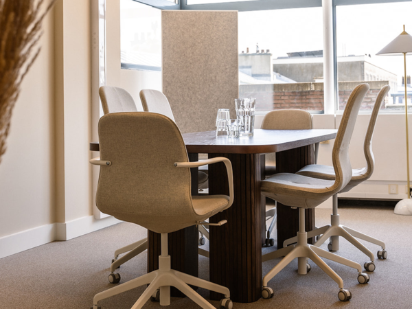 Moderne vergaderruimte met een houten tafel, vier beige stoelen en glazen karaffen.