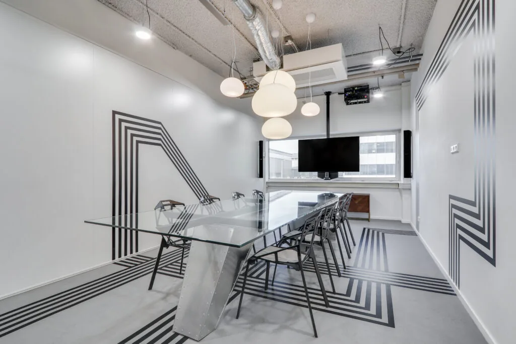 Moderne vergaderruimte met glazen tafel, industriële details en zwart-wit lijnpatroon op vloer en muren.