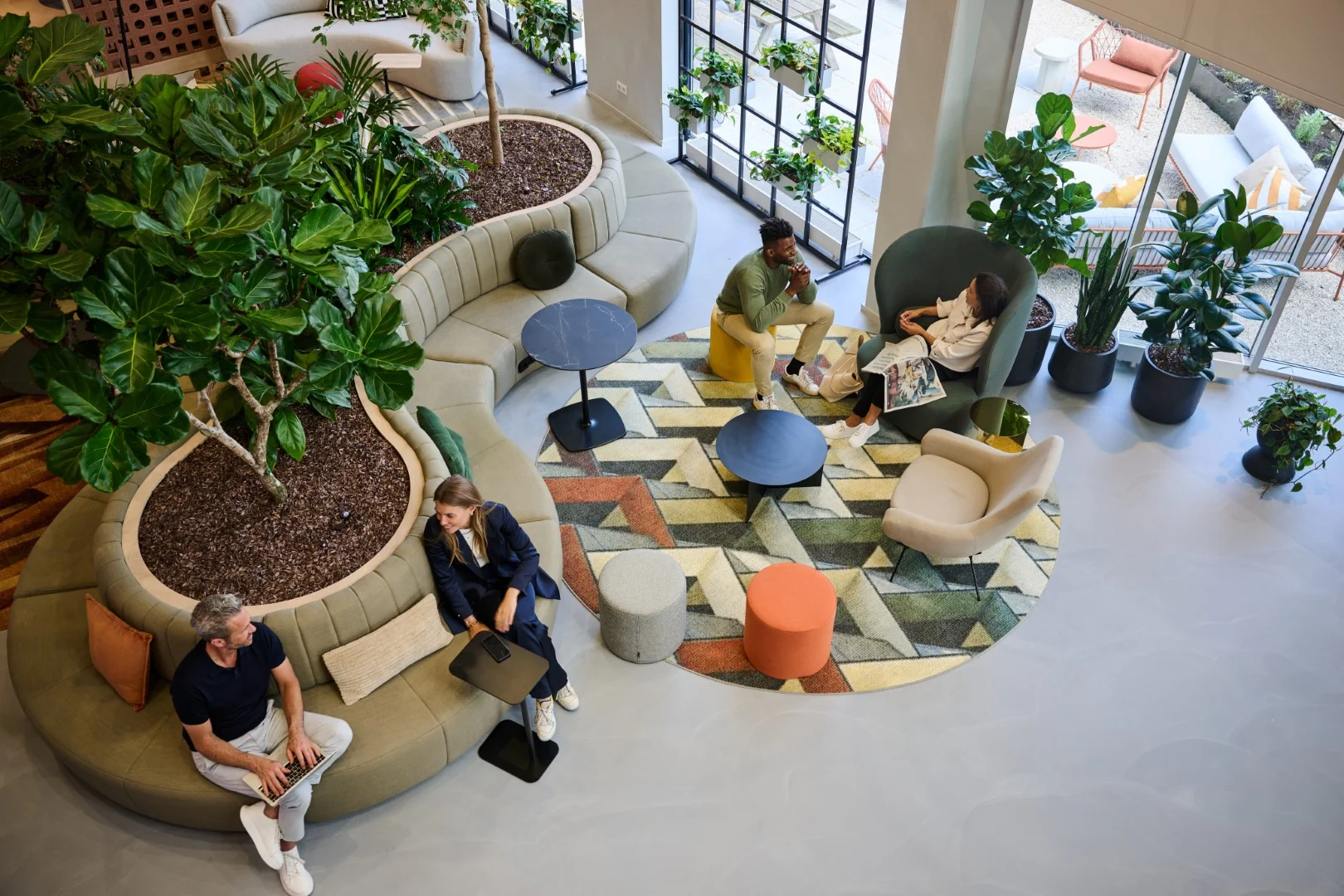 Moderne loungeruimte met planten, kleurrijke meubels en mensen in gesprek of aan het werk.