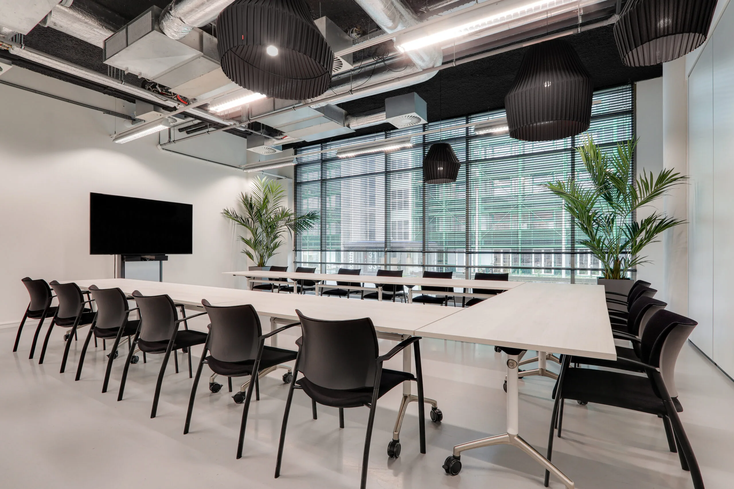 Moderne vergaderruimte in Den Haag met opstelling in U-vorm, zwarte stoelen, grote ramen en een flatscreen.