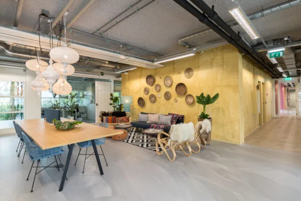 Moderne en kleurrijke lounge- en werkruimte in HNK Amsterdam Zuidoost met houten tafel, designverlichting en gele accentmuur.