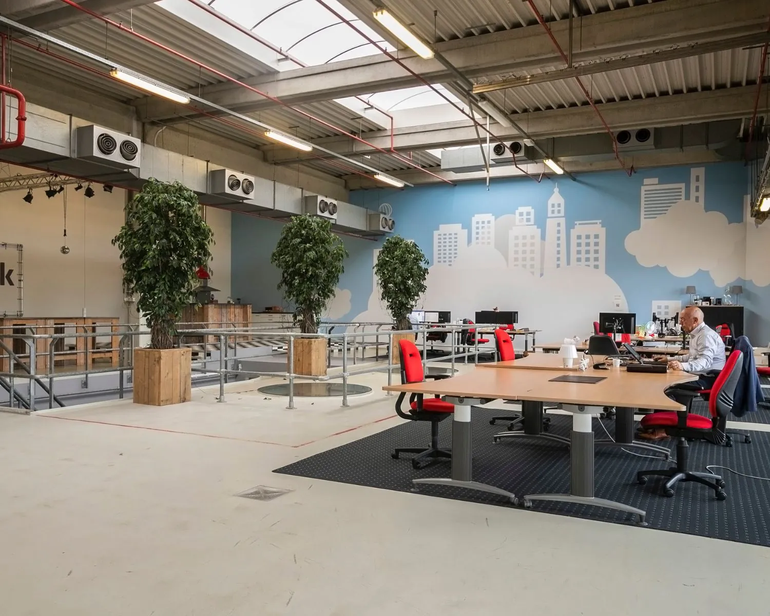 Moderne kantoorruimte aan de Bolderweg 2 in Almere met open werkplekken, rode bureaustoelen en muurschildering van een stadsgezicht.