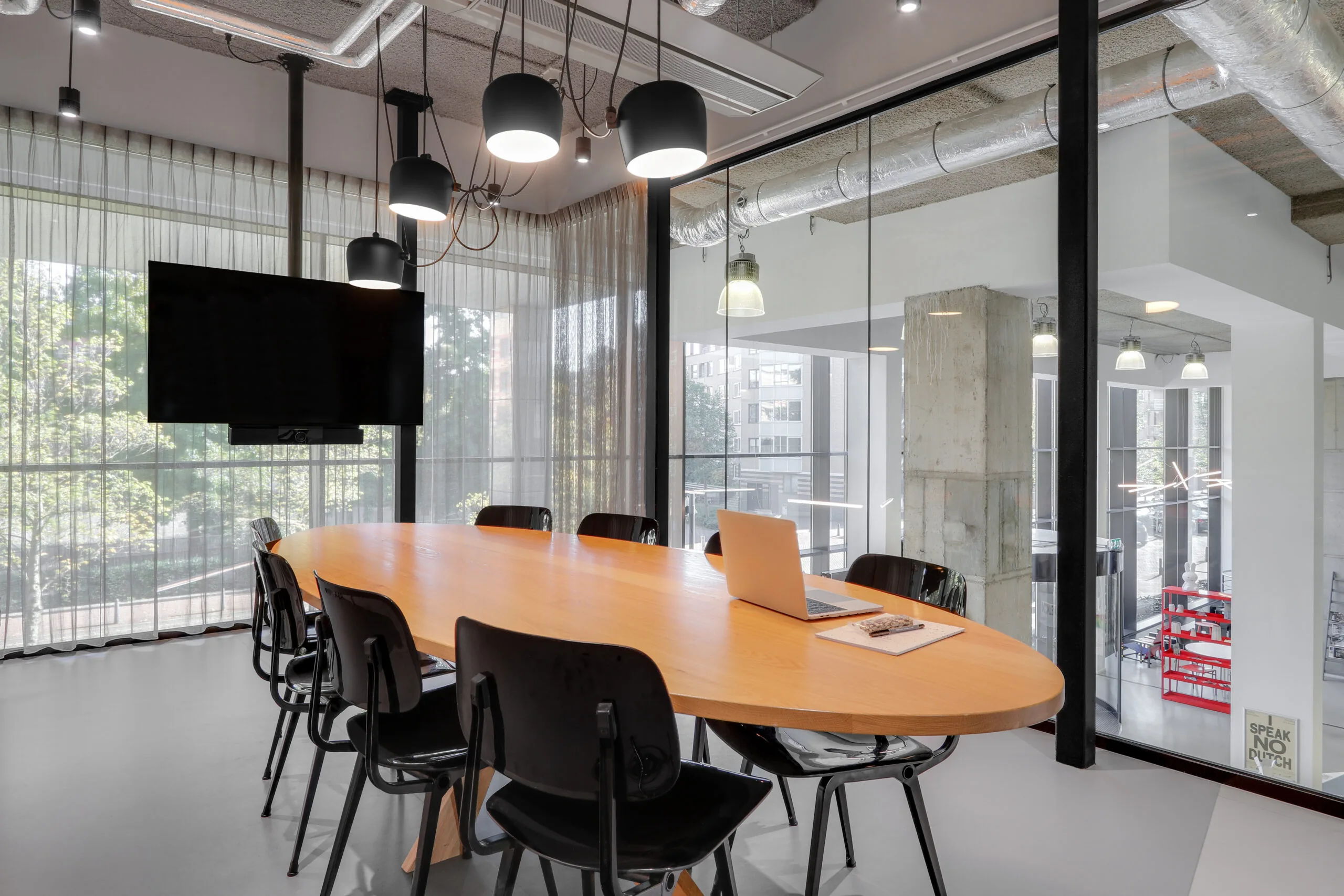 Moderne vergaderruimte in Utrecht Centraal met een ovale houten tafel, zwarte stoelen, hanglampen en een laptop op tafel.