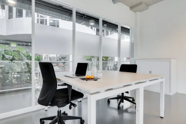 Moderne en lichte werkplek in Utrecht West met twee bureaustoelen, een laptop, een karaf water en uitzicht op een binnentuin.
