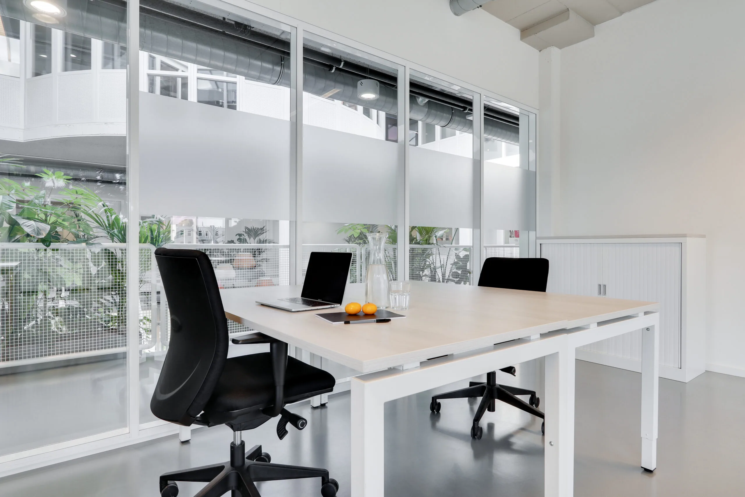 Moderne en lichte werkplek in Utrecht West met twee bureaustoelen, een laptop, een karaf water en uitzicht op een binnentuin.