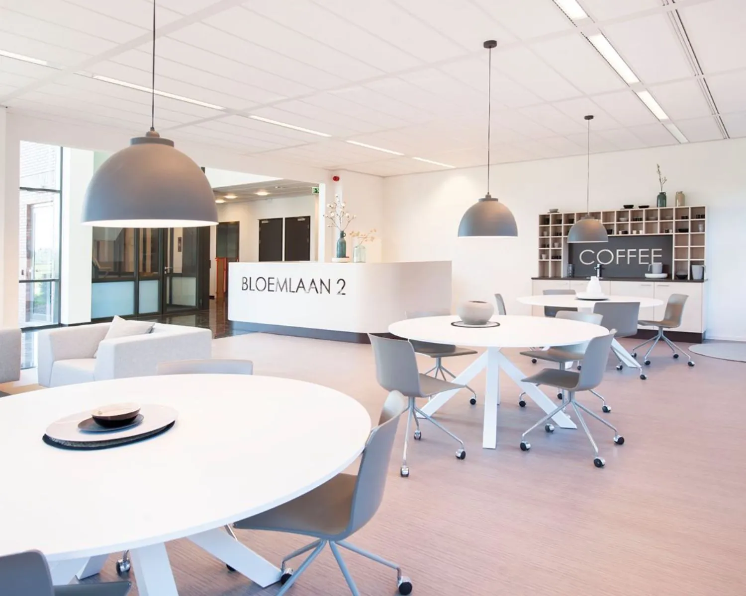 Moderne kantoorruimte met zitgedeelte, ronde vergadertafels en een koffiehoek aan de Bloemlaan 2 in Hoofddorp.