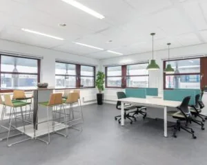 Moderne, lichte kantoorruimte te huur aan het Capitool 10 in Enschede met werkplekken, een hoge zittafel en grote ramen.