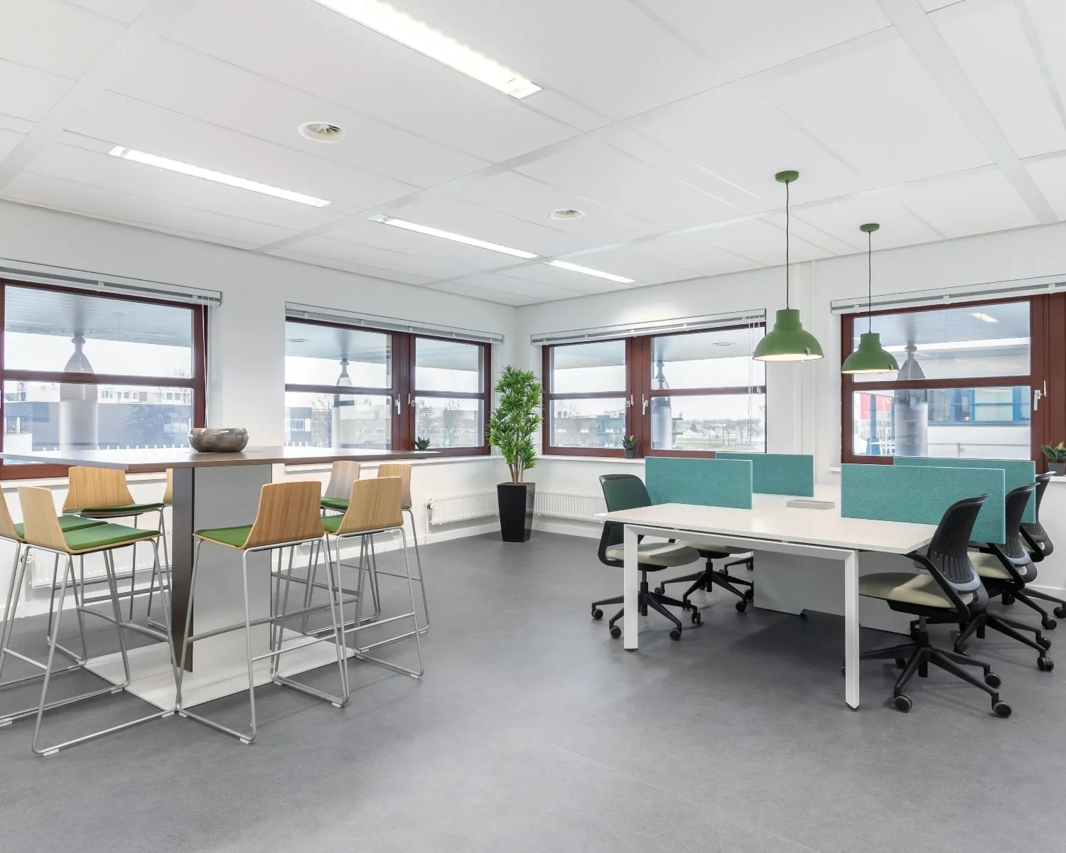 Moderne, lichte kantoorruimte te huur aan het Capitool 10 in Enschede met werkplekken, een hoge zittafel en grote ramen.