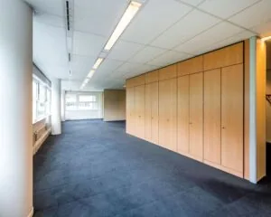 Lichte kantoorruimte te huur aan Entrada 300 in Amsterdam met grote ramen, donker tapijt en een houten kastenwand.