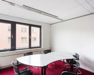 Kleine vergaderruimte met moderne bureaus, vier stoelen en grote ramen aan de Kronenburgsingel 525 in Arnhem.
