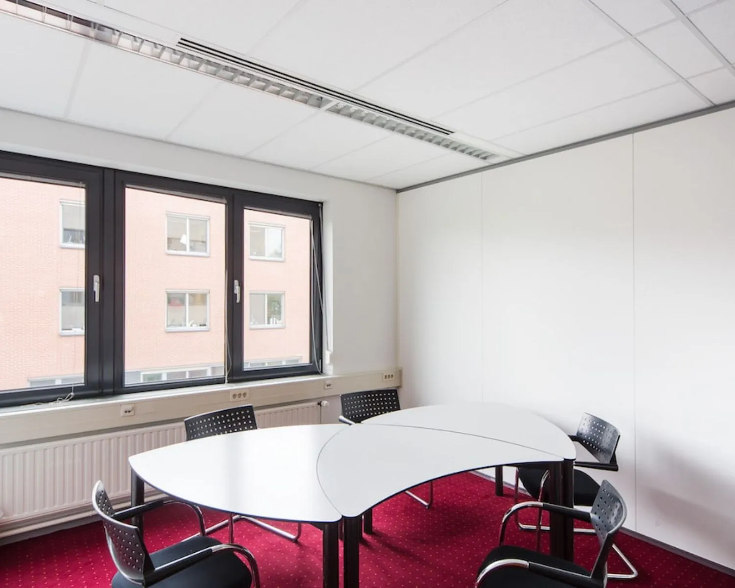 Kleine vergaderruimte met moderne bureaus, vier stoelen en grote ramen aan de Kronenburgsingel 525 in Arnhem.
