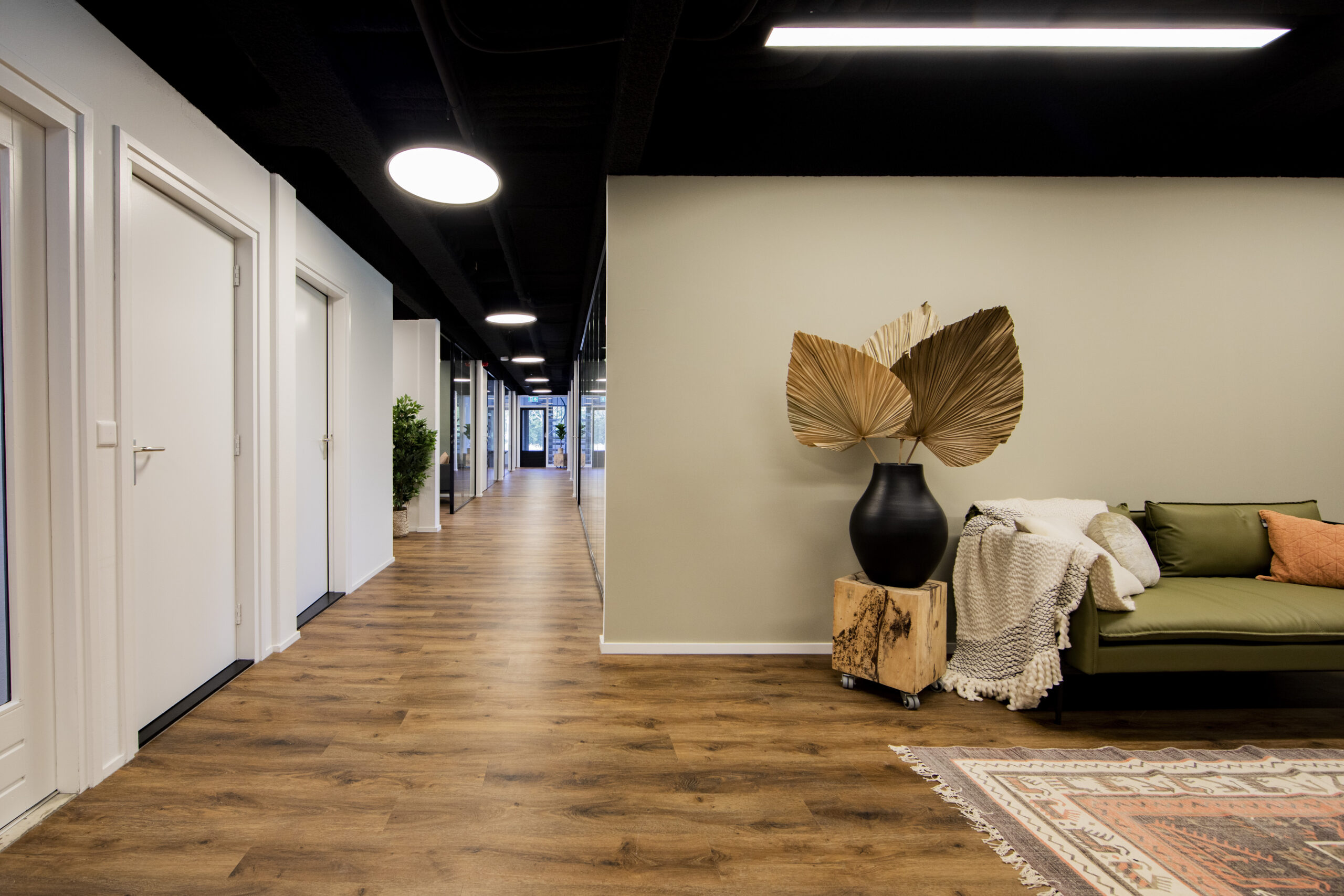 Een moderne kantoorhal met houten vloer, planten en comfortabele zithoek in ELE Office Woerden.