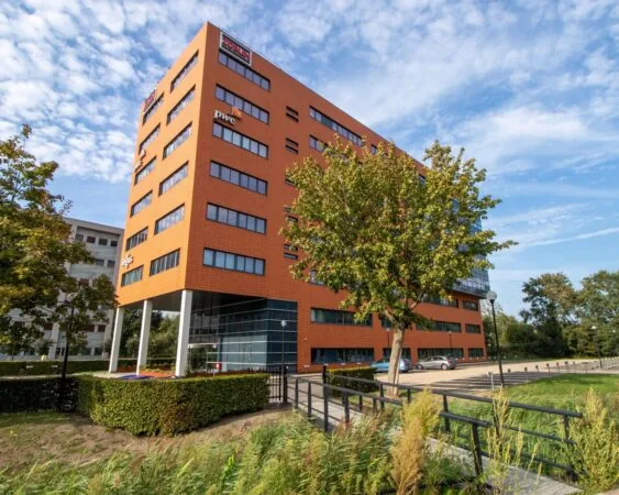 Modern kantoorgebouw 5018_1 met oranje gevel en logo's van onder andere PWC, omringd door groen en een parkeerplaats.