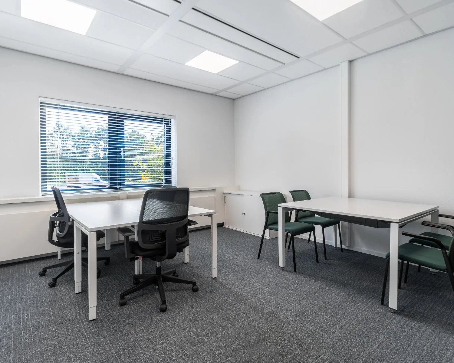 Kantoorruimte met twee bureaus, bureaustoelen en vergaderstoelen in een lichte, moderne inrichting.