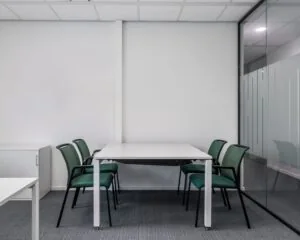 Moderne vergaderruimte met een witte tafel en vier groene stoelen in een minimalistisch kantoorinterieur.