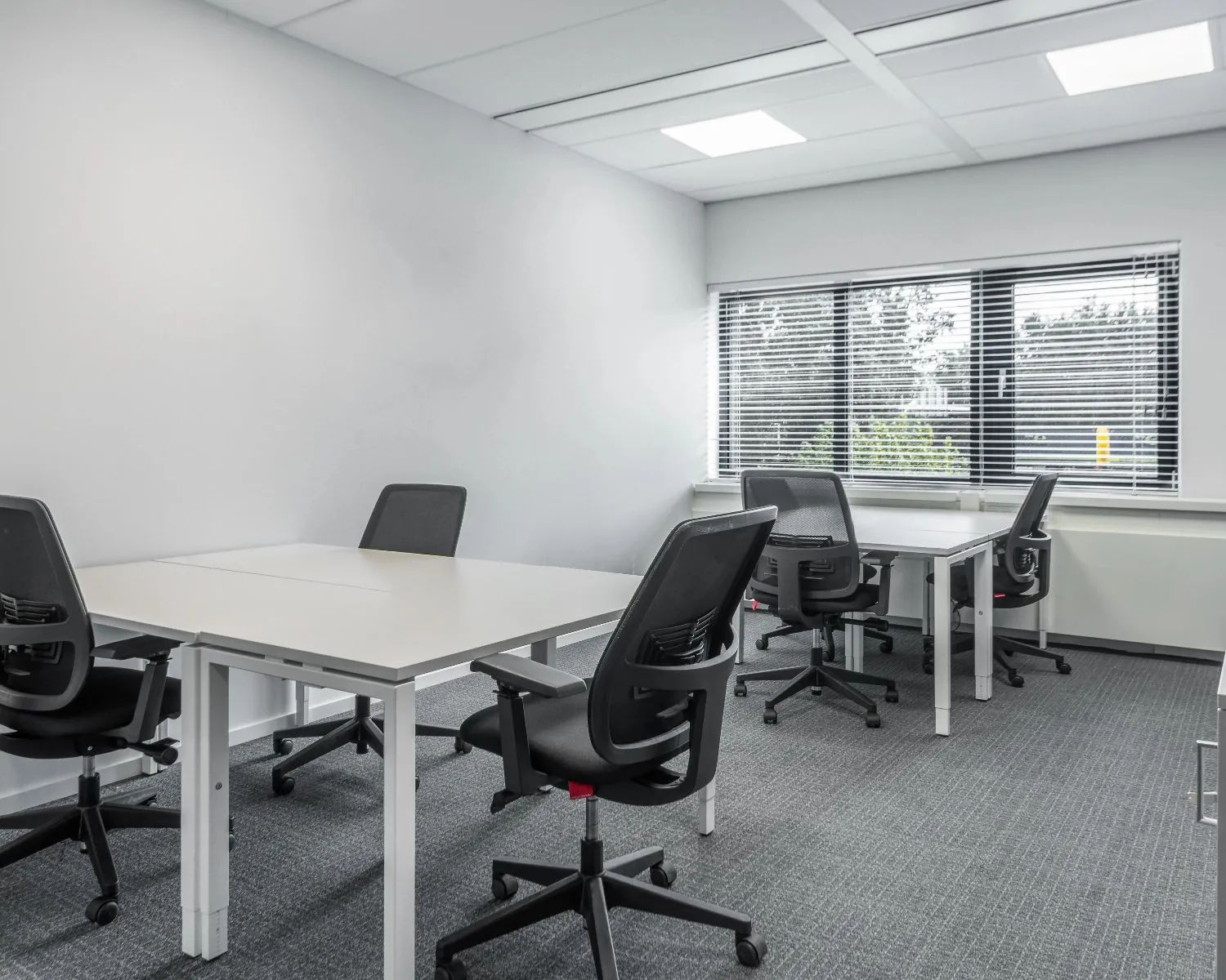 Moderne, lichte kantoorruimte met zes bureaus en ergonomische bureaustoelen in een neutraal interieur.