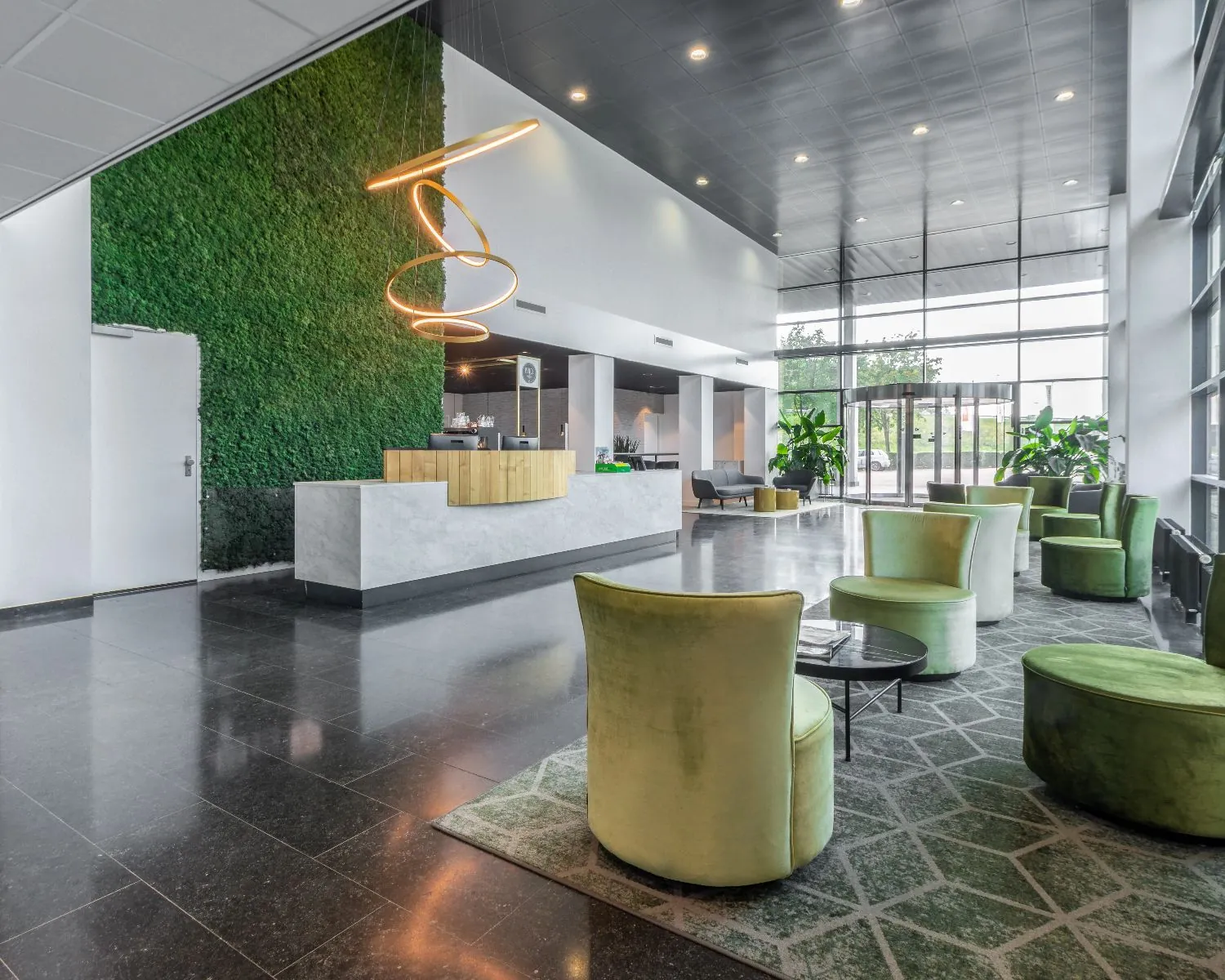 Moderne hotellobby met een groene moswand, designverlichting en groene fauteuils bij de receptie.
