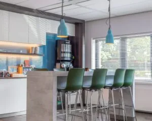 Moderne keukenhoek met een hoge betonnen tafel, groene barkrukken en een Nespresso koffiemachine.