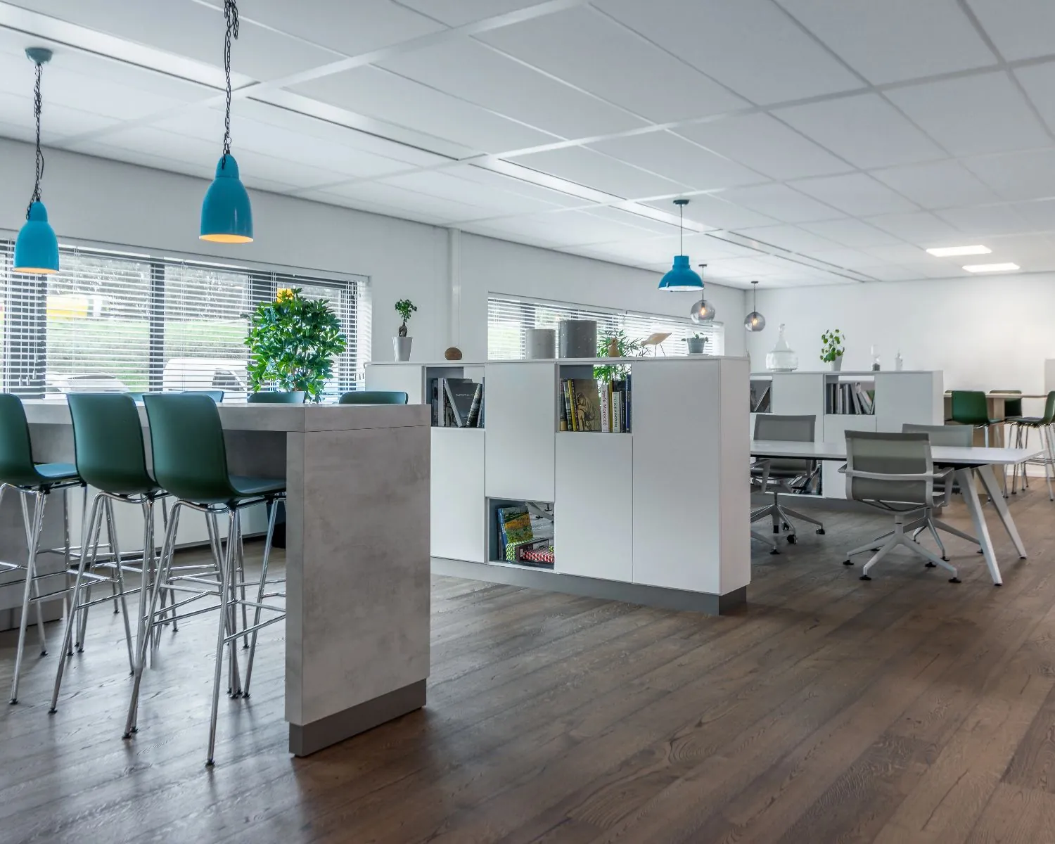 Moderne en open kantoorruimte met hoge stoelen, witte kasten, bureaus en hanglampen.