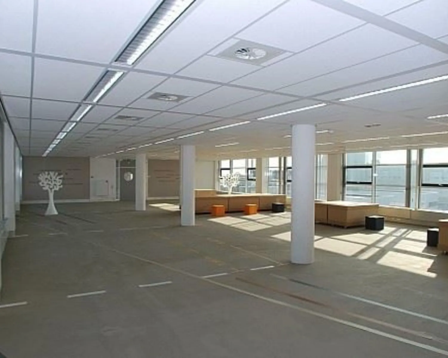 Ruime, moderne kantoorruimte met grote ramen, zitblokken en decoratieve elementen zoals witte boomfiguren.
