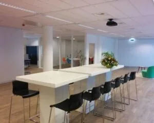 Moderne kantoorruimte met een hoge witte tafel, zwarte barkrukken en een bloemstuk als middelpunt.