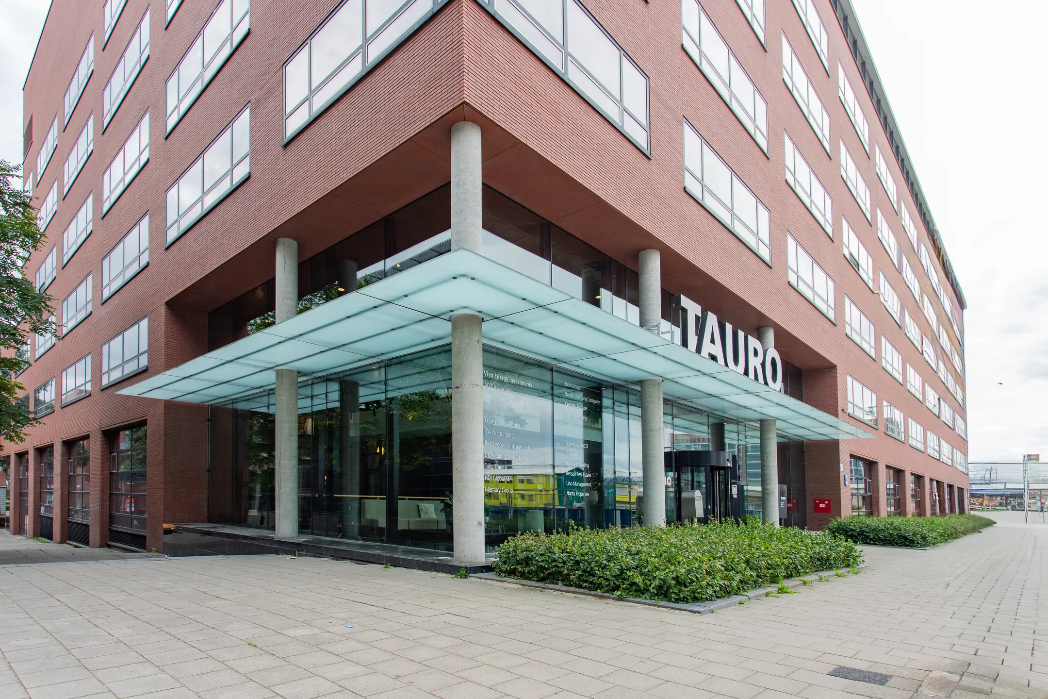 Onderhoek van een rood bakstenen kantoorgebouw met de naam "TAURO" bij de ingang.
