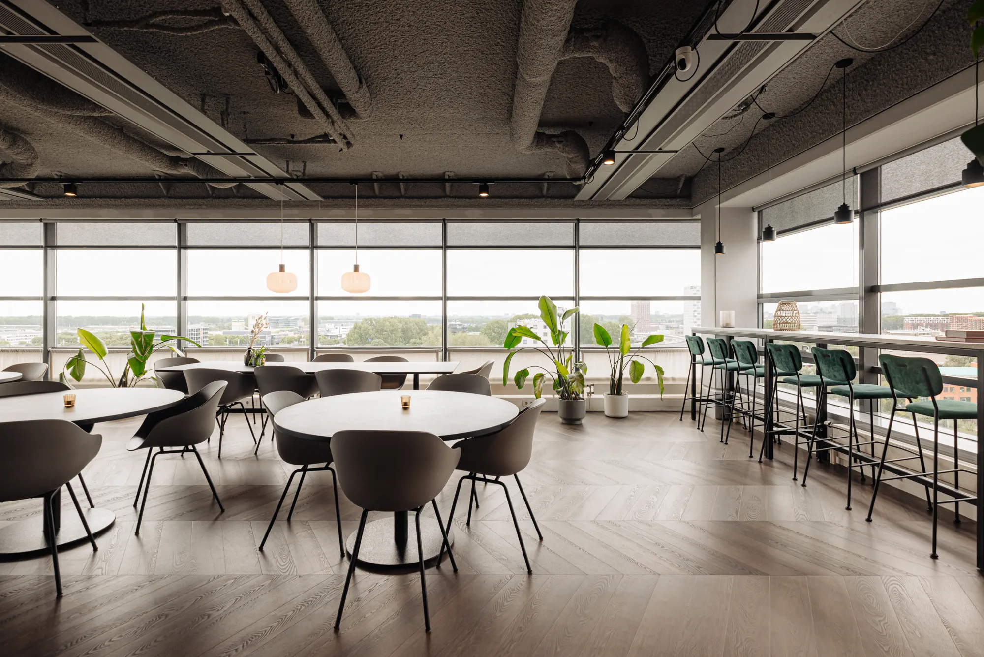 Een moderne, lichte kantoorruimte met ronde tafels, stoelen en hoge krukken bij grote ramen.