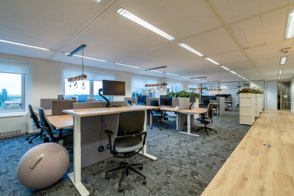Moderne kantoorruimte met open werkplekken, ergonomische bureaus en veel natuurlijk licht.