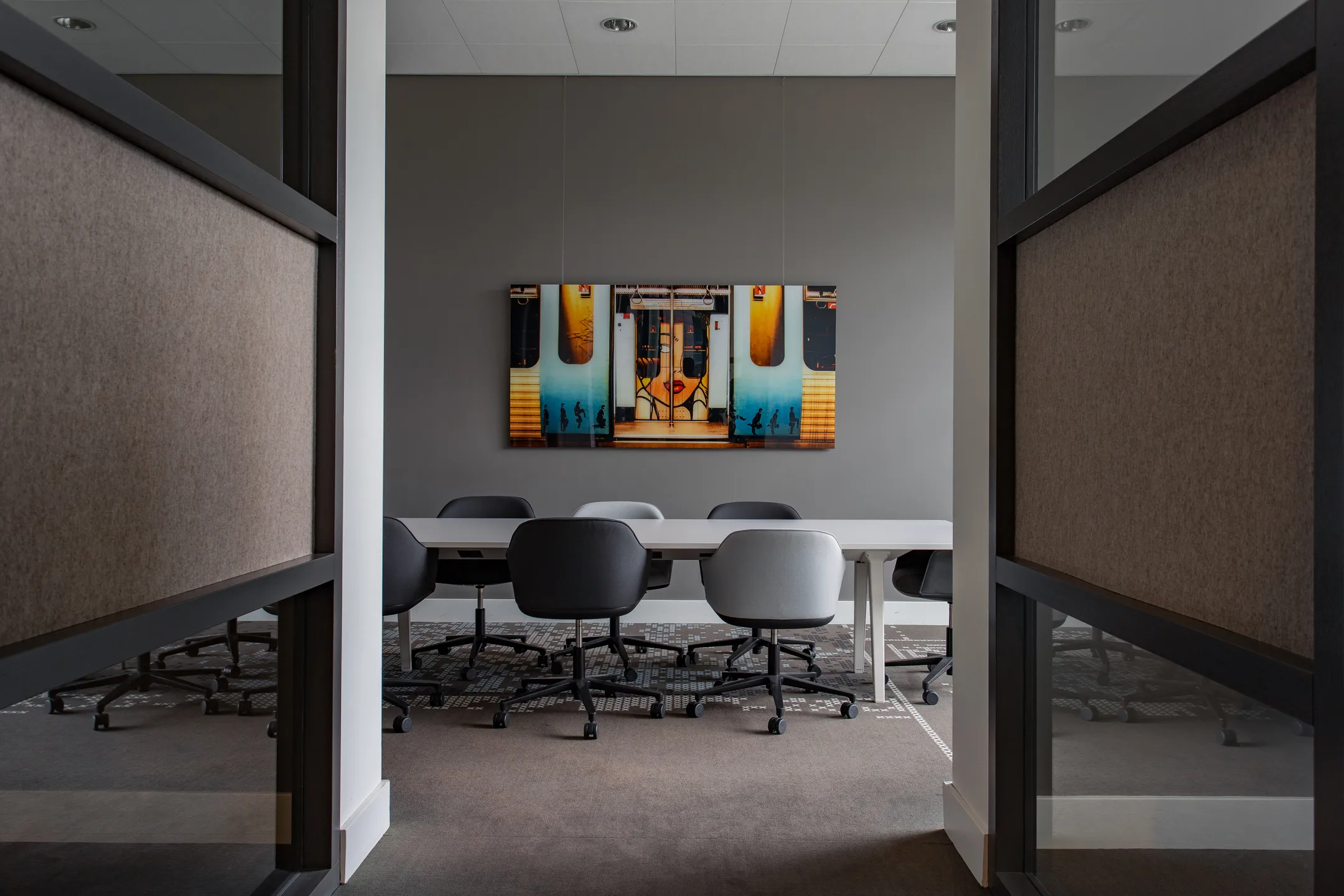 Vergaderruimte met een lange tafel, stoelen en een kleurrijk kunstwerk aan de muur.