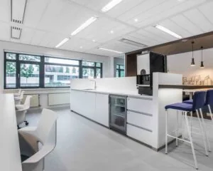 Moderne, lichte kantoorkeuken met een koffieautomaat, barkrukken en grote ramen.