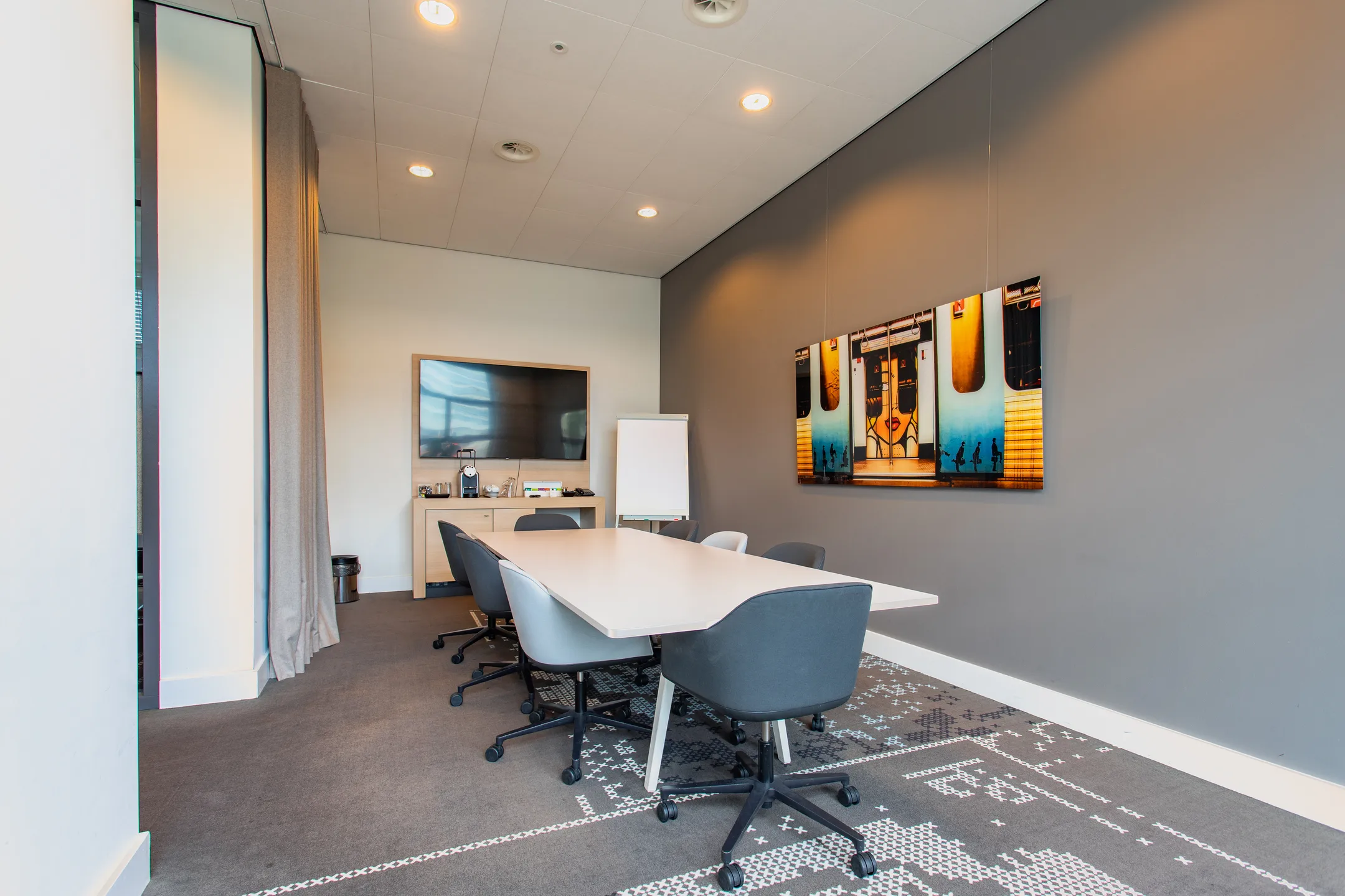 Vergaderruimte met een lange tafel, stoelen en een kunstwerk aan de muur.