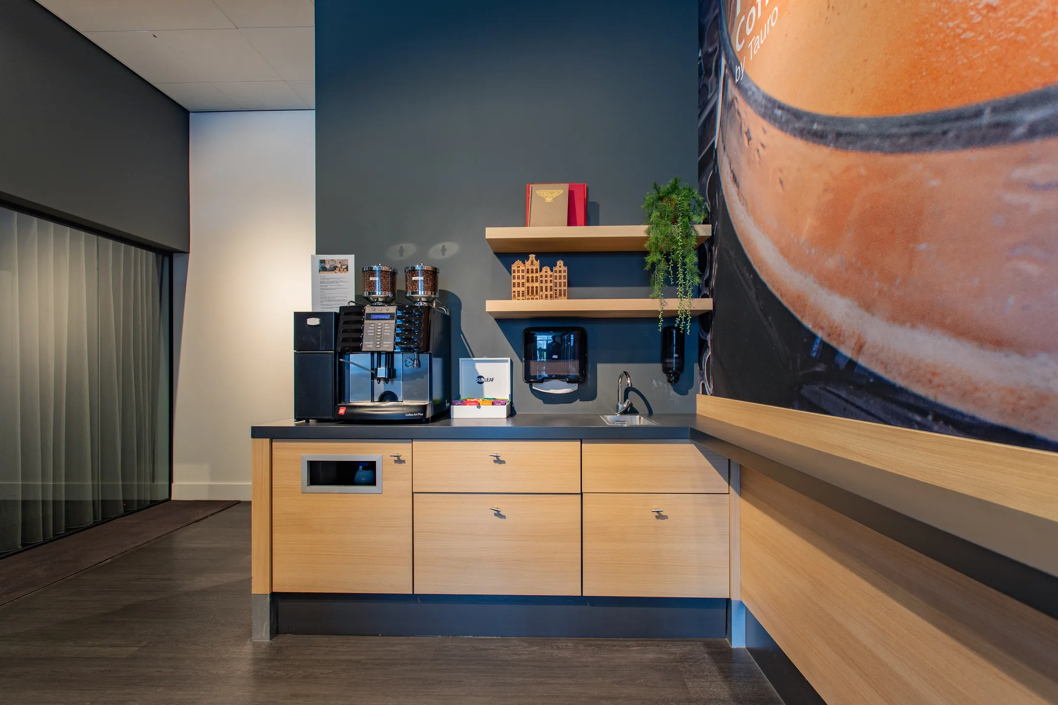 Een moderne koffiehoek met een koffiemachine, houten kasten, planken en een grote muurfoto van koffie.