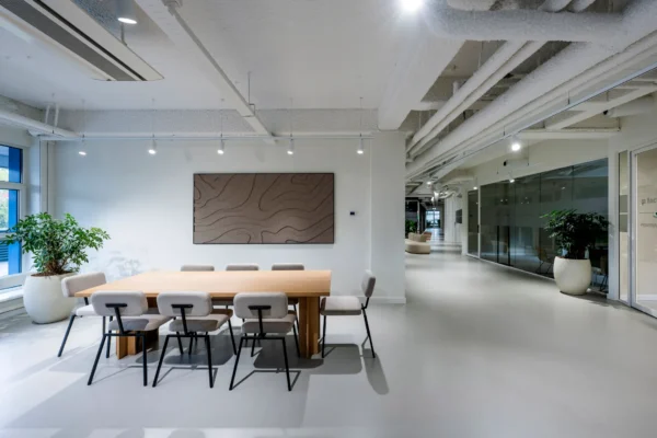 Een moderne vergaderruimte met een houten tafel, beige stoelen, planten en kunst aan de muur.