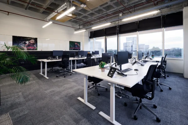 Een modern en ruim kantoor met bureaus, computers en grote ramen met uitzicht op gebouwen.