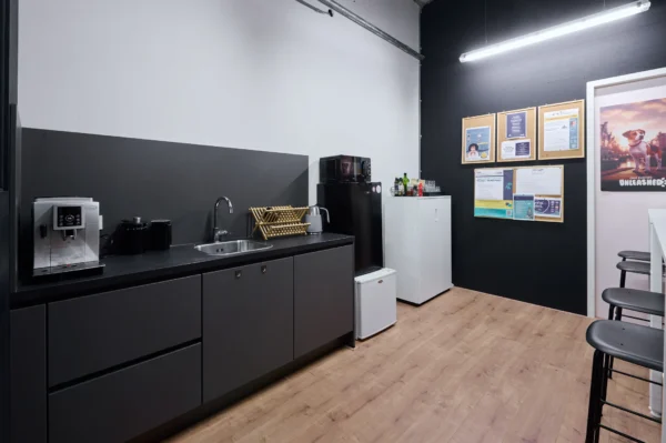 Een moderne kantoorkeuken met een koffiezetapparaat, gootsteen, magnetron, koelkast en informatieve mededelingen aan de muur.