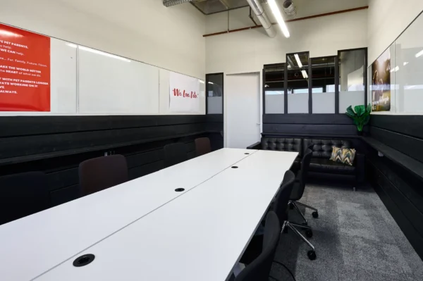 Moderne vergaderruimte met een lange witte tafel, zwarte stoelen, en decoratieve posters aan de muur.