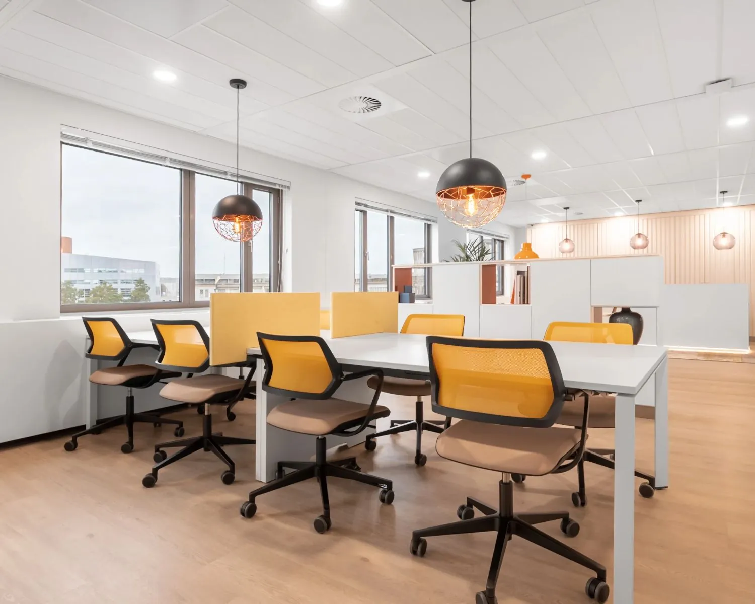Modern kantoorinterieur met gedeelde werkplekken, gele bureaustoelen en hanglampen in een lichte ruimte.
