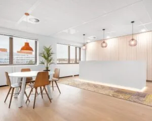 Moderne en lichte kantoorruimte met een witte balie, houten vloer, ronde vergadertafel en hanglampen.