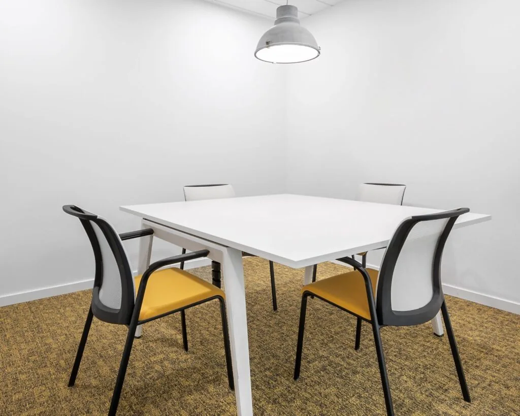 Minimalistisch vergaderruimte met een witte tafel, vier moderne stoelen en een industriële hanglamp.